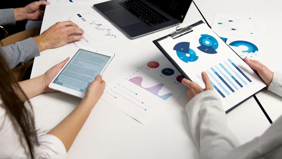 Un espace de travail contemporain où des mains examinent des données marketing sur un ordinateur portable et des documents papier.